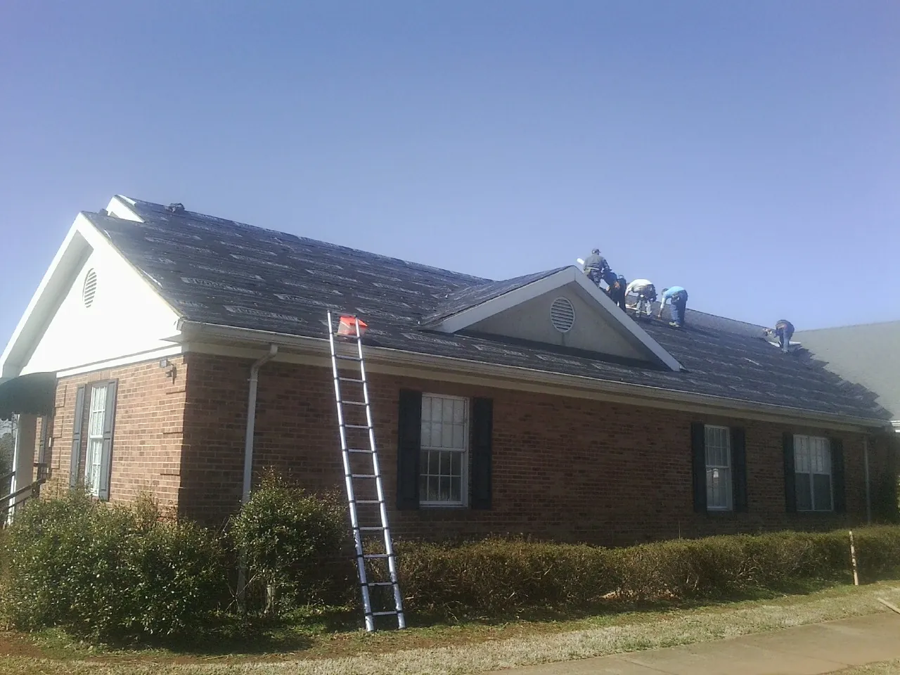 Crew tearing shingles off a brick ranch roof with a ladder set — Emergency Roof Repair work by our crew in Vantage