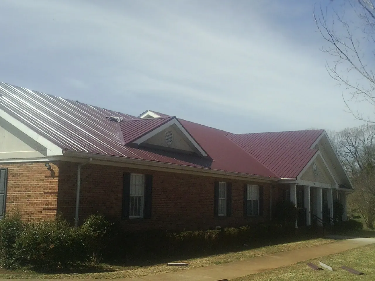 Red metal roof with gabled entries on a long brick building, from a Hail Damage Roof Repair job in Vantage