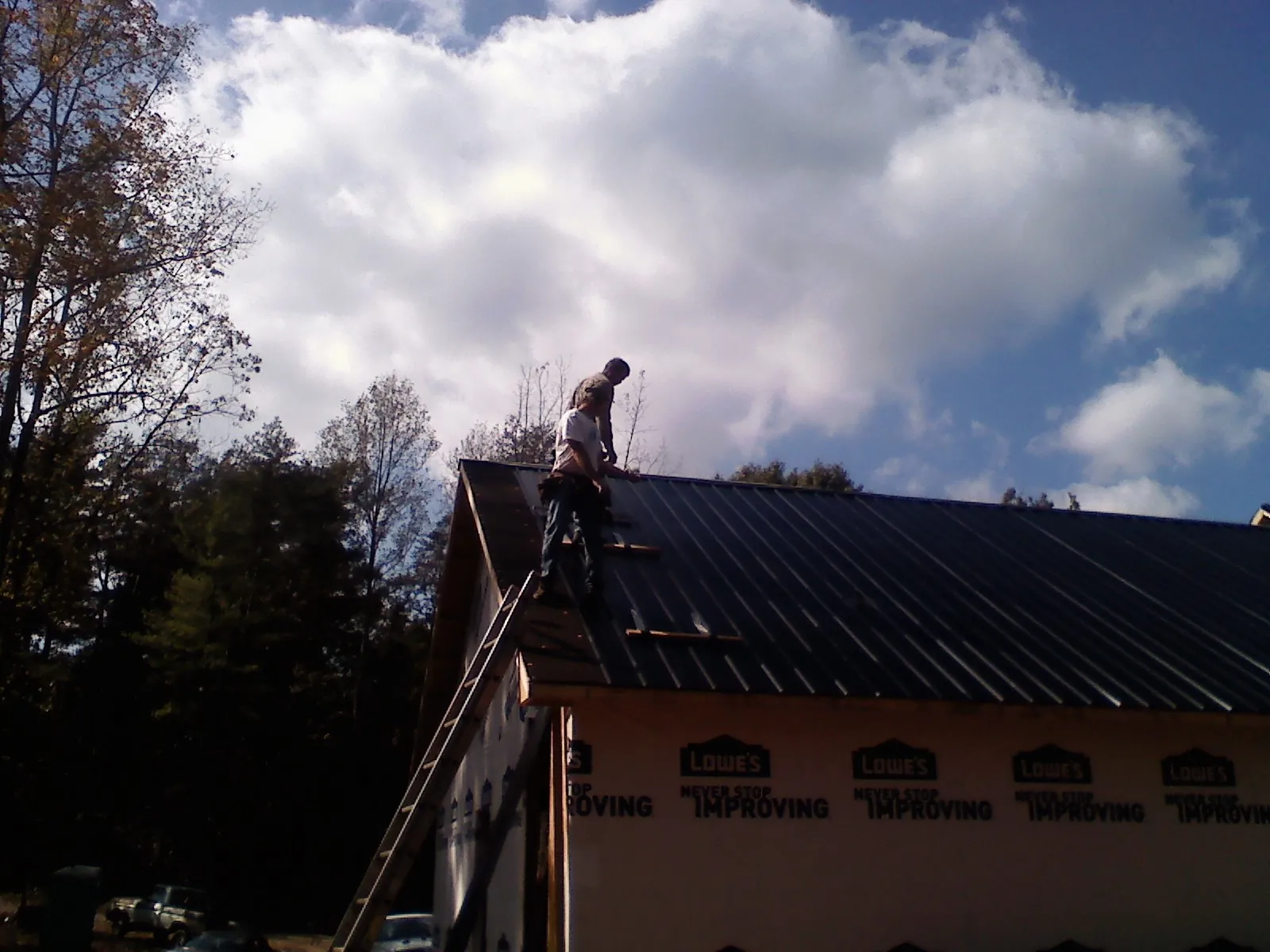 Roofer fastening dark metal panels high against a cloudy sky, from a Roof Inspection job in Vantage